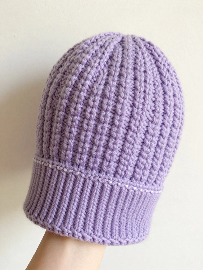 Handheld purple ribbed crochet beanie with white brim trim against a plain background