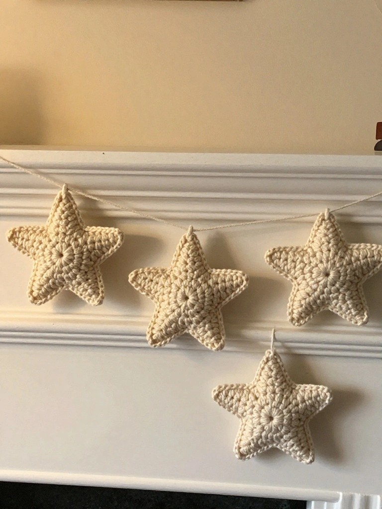 Handmade beige crochet stars strung on twine, hanging across a white mantel above a dark fireplace hearth.