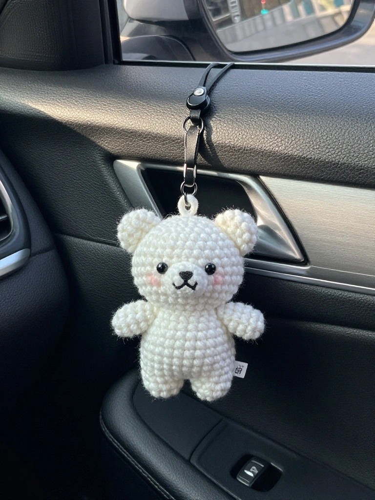 A white crocheted bear keychain hanging from a car's dashboard.