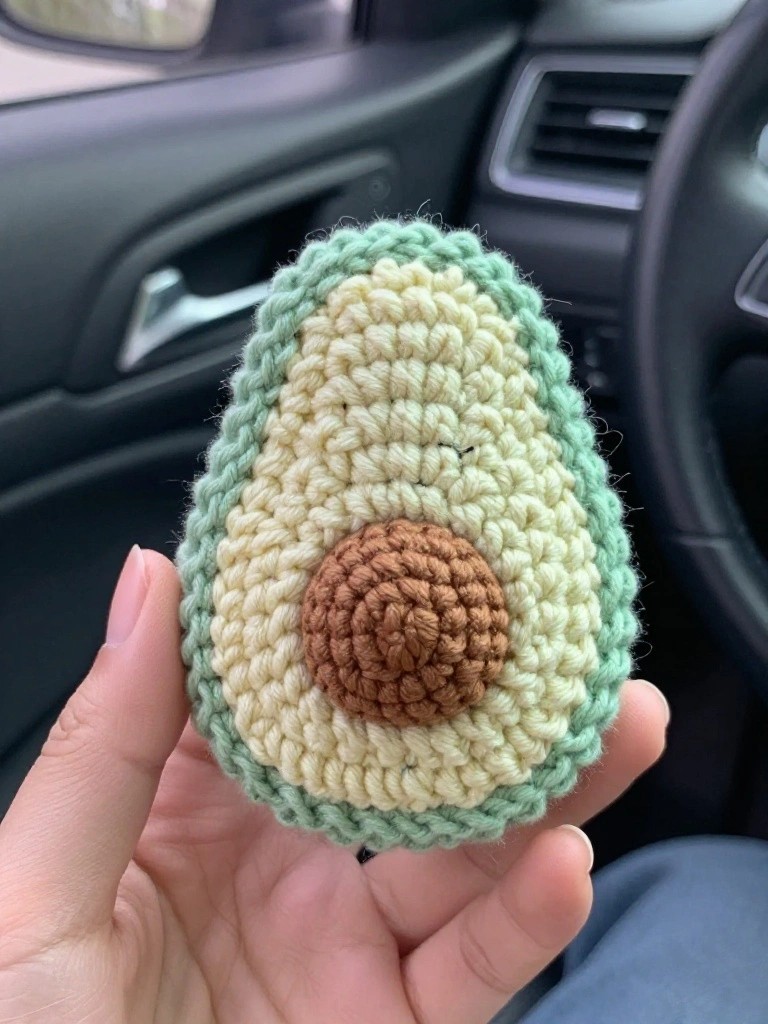 Crocheted avocado plush toy held in a hand inside a car.