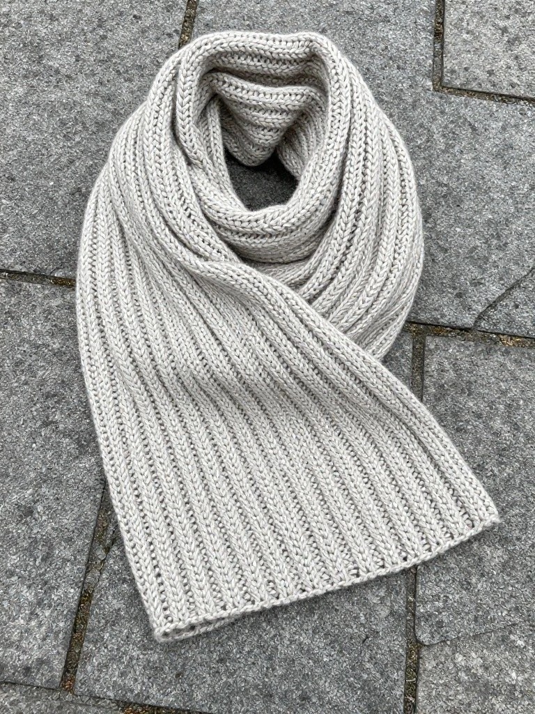 Light gray ribbed knit scarf looped on gray stone pavement