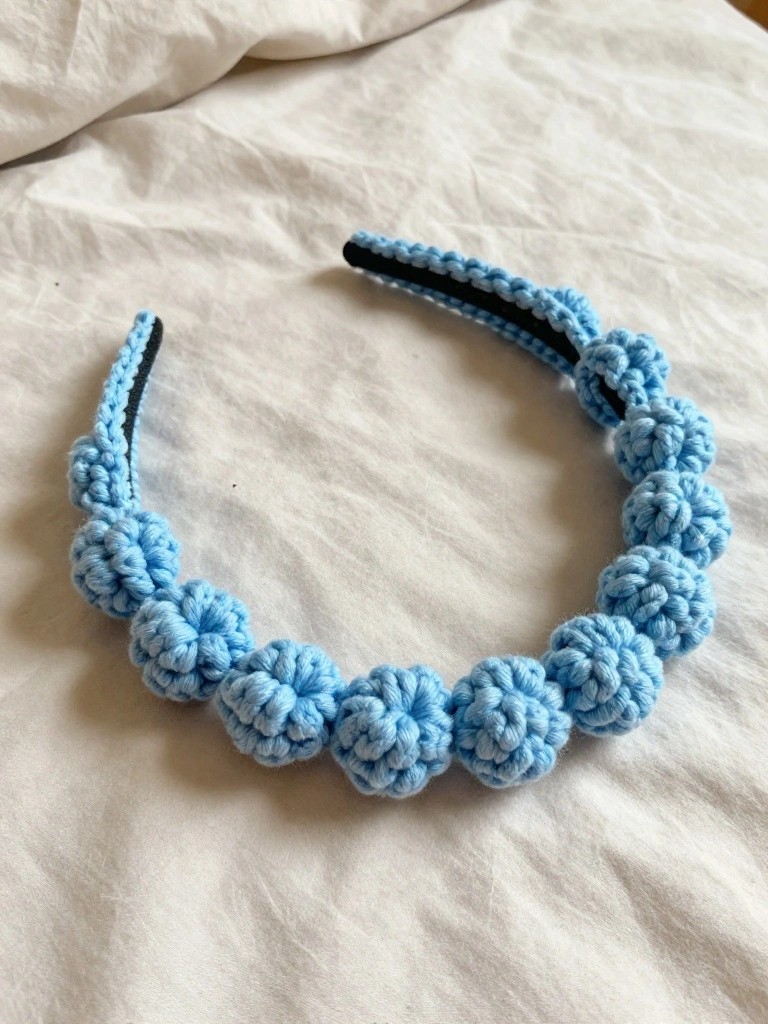 Light blue crocheted floral headband on wrinkled white fabric.
