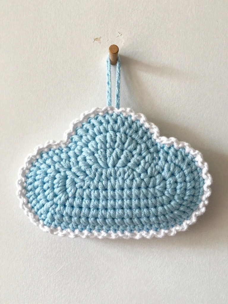 Light blue crocheted cloud with white trim hanging from wooden peg on wall