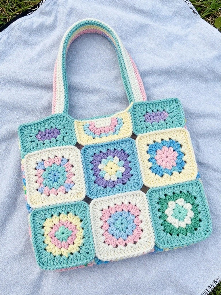 Pastel granny square crochet tote bag with striped handle on blue fabric