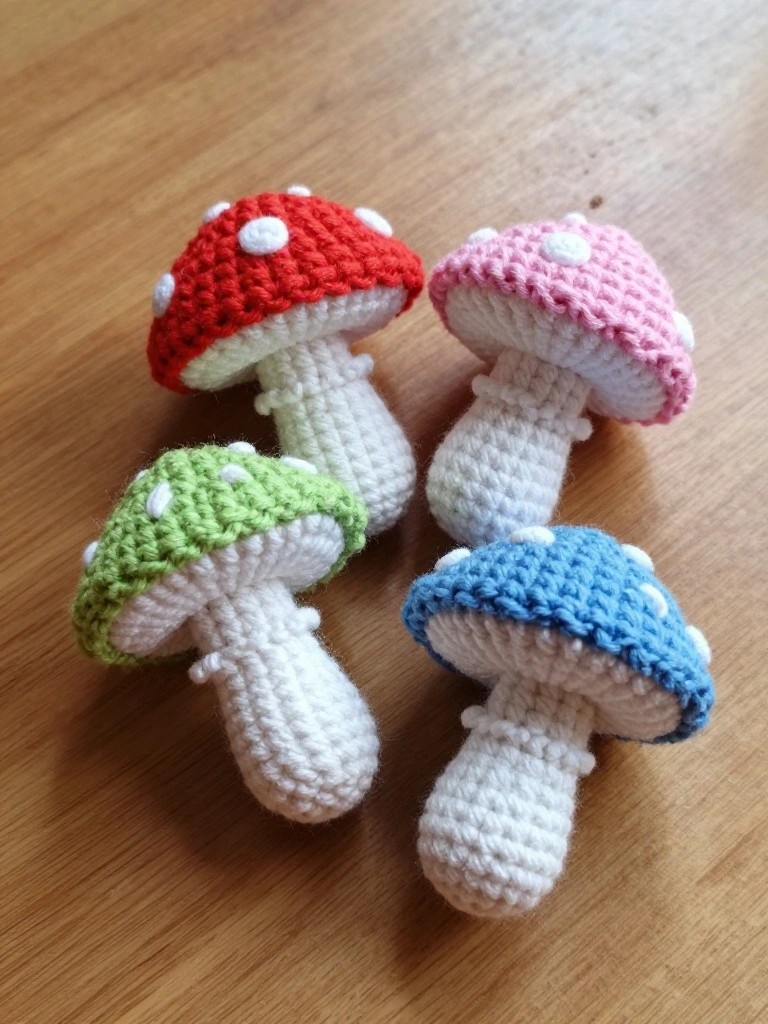 Four colorful crocheted mushrooms with spotted caps and white stems on wood.
