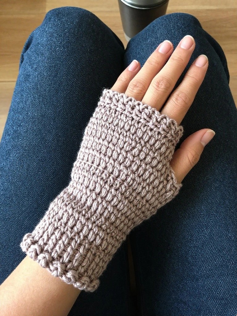 Hand in dusty pink knitted fingerless glove resting on blue denim jeans