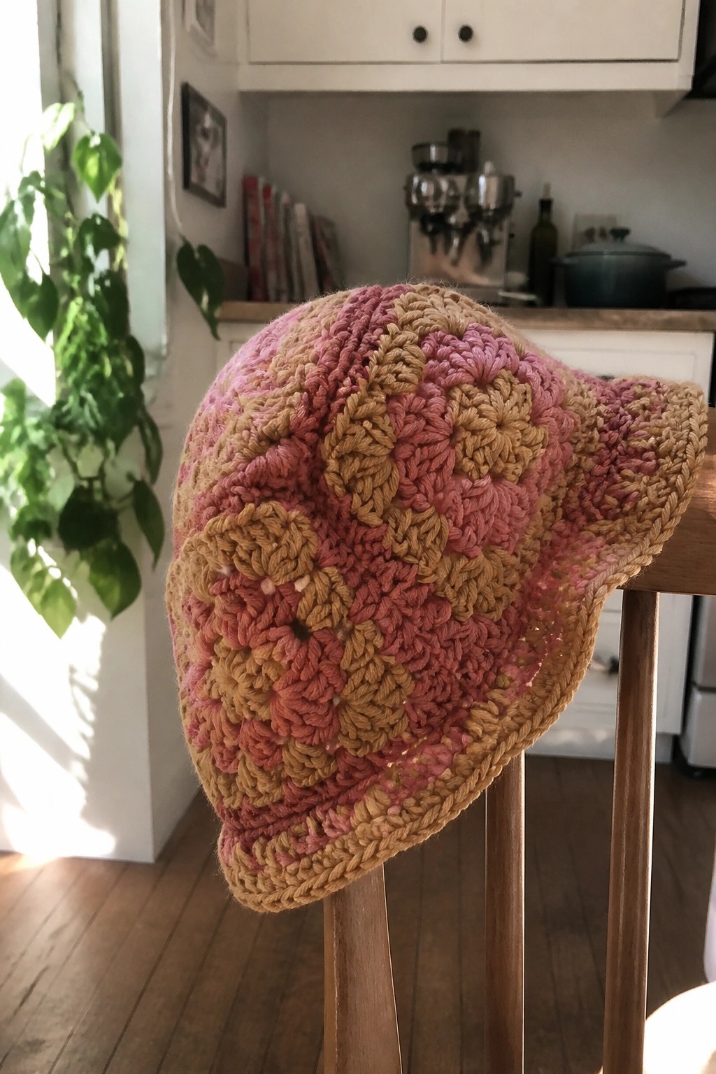 Crocheted bucket hat made from pink and brown granny squares on a wooden chair.