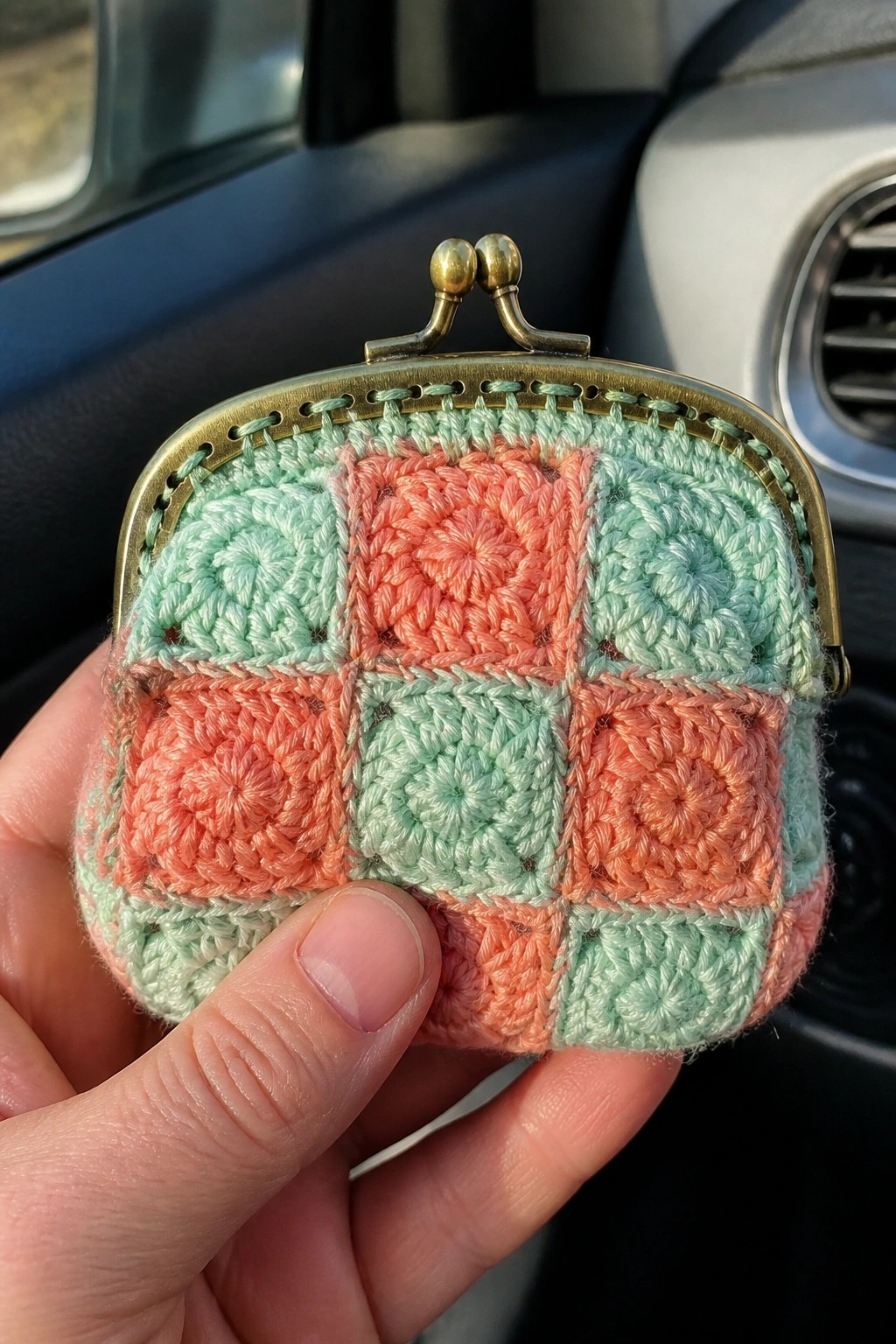 Hand holding crocheted coin purse of mint green and coral granny squares.
