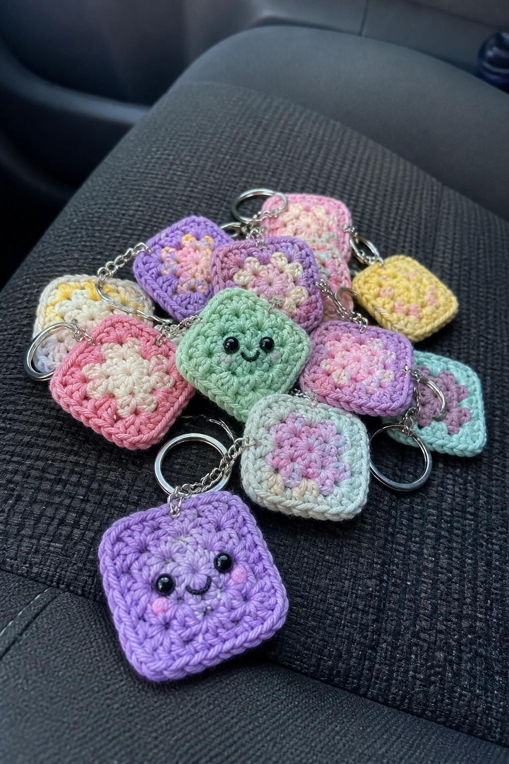 Colorful crocheted granny square keychains with faces piled on gray car seat