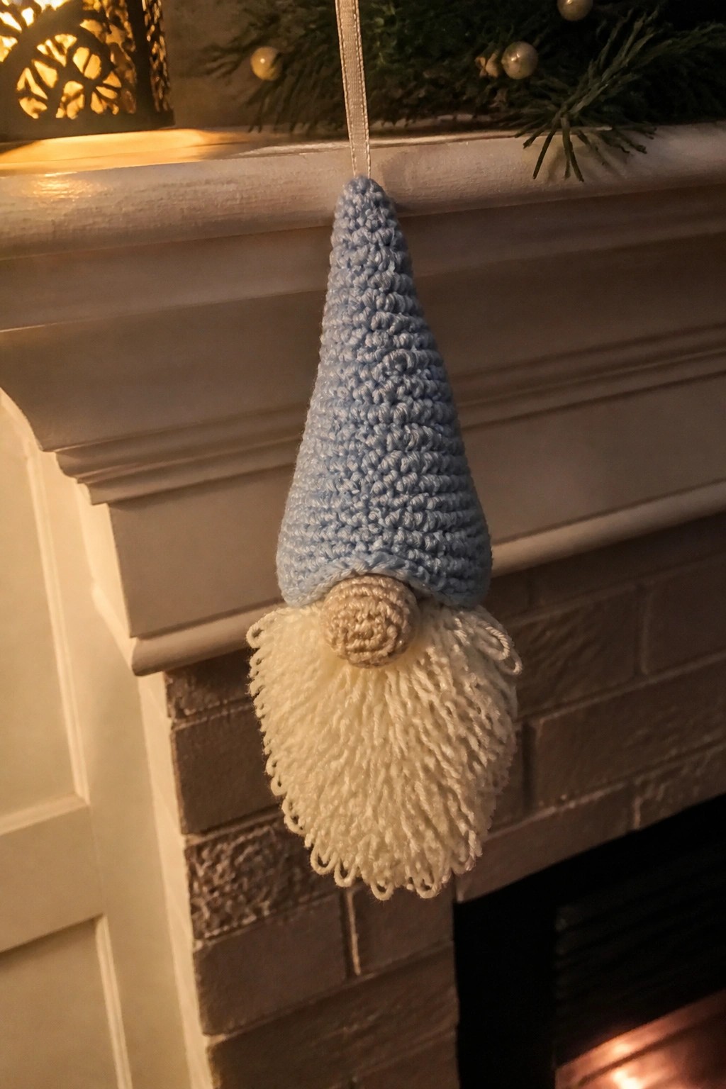 Crocheted light blue gnome with fluffy white beard hanging from fireplace mantel.