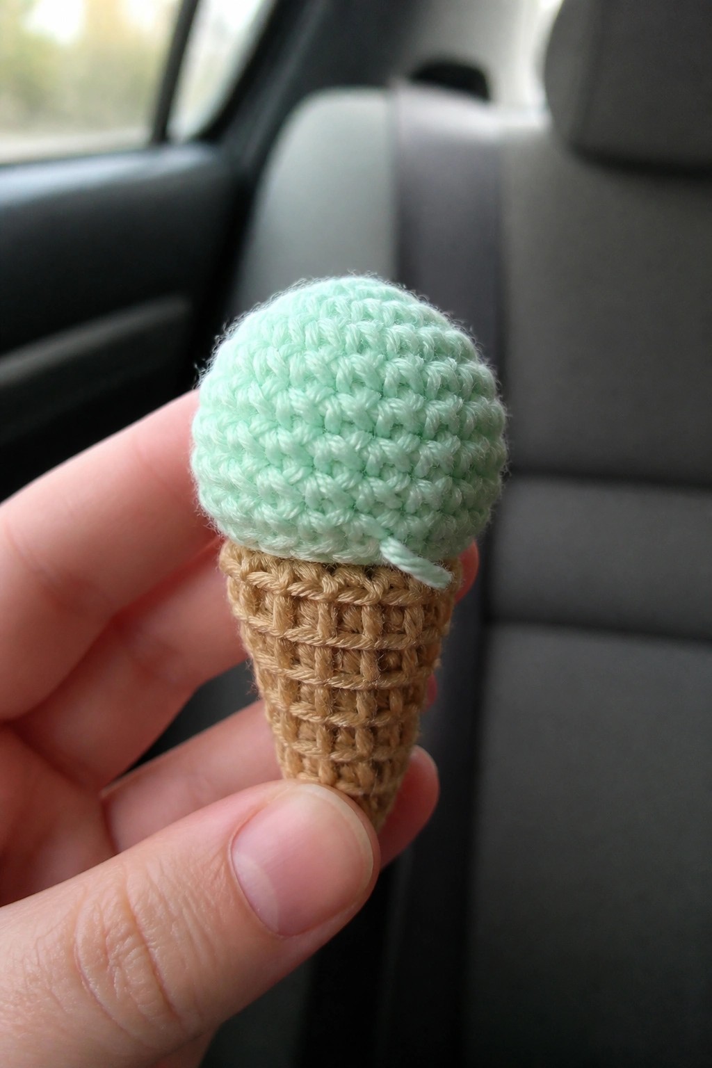 Hand holding crocheted mint green ice cream cone inside a car