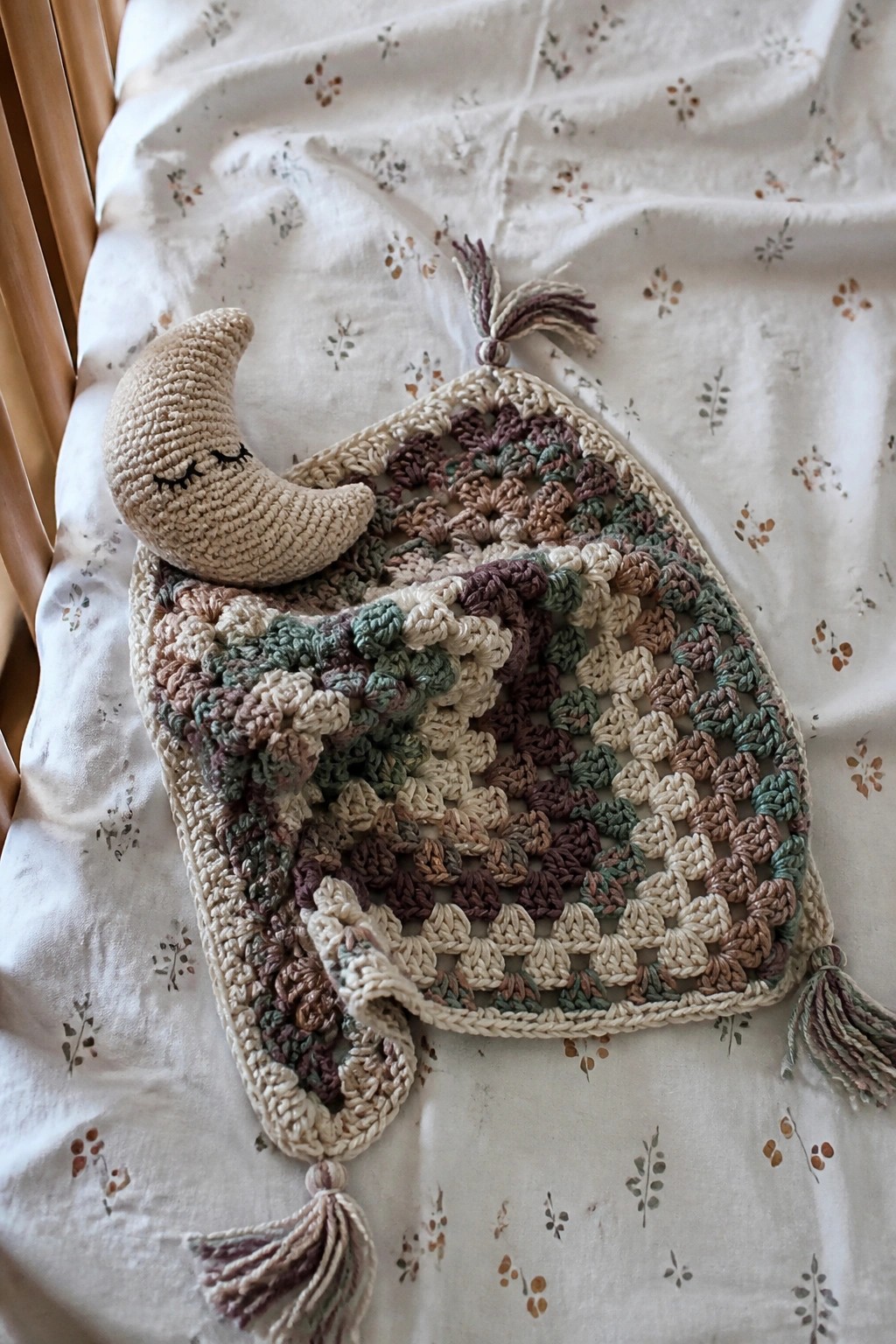 Crocheted granny square blanket with moon toy and tassels on floral sheet