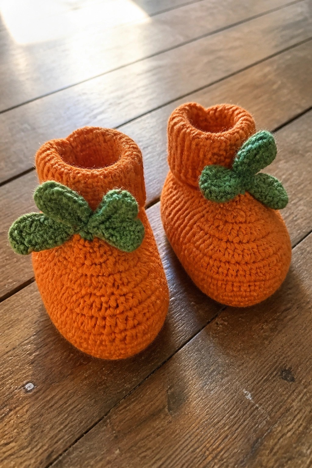Two orange crocheted baby booties with green leaves on wooden floor