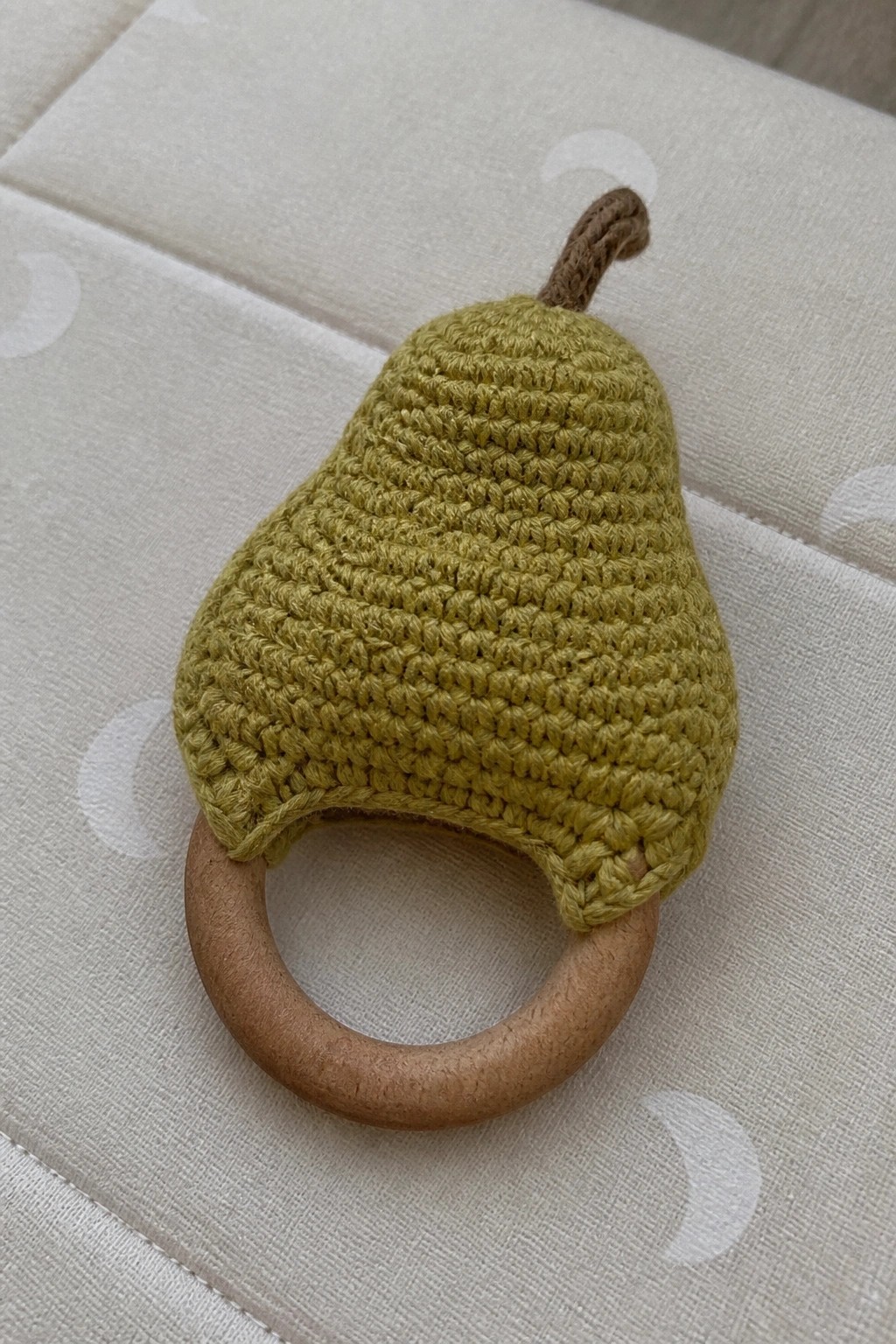 Green crocheted pear teether with wooden ring and brown stem on fabric