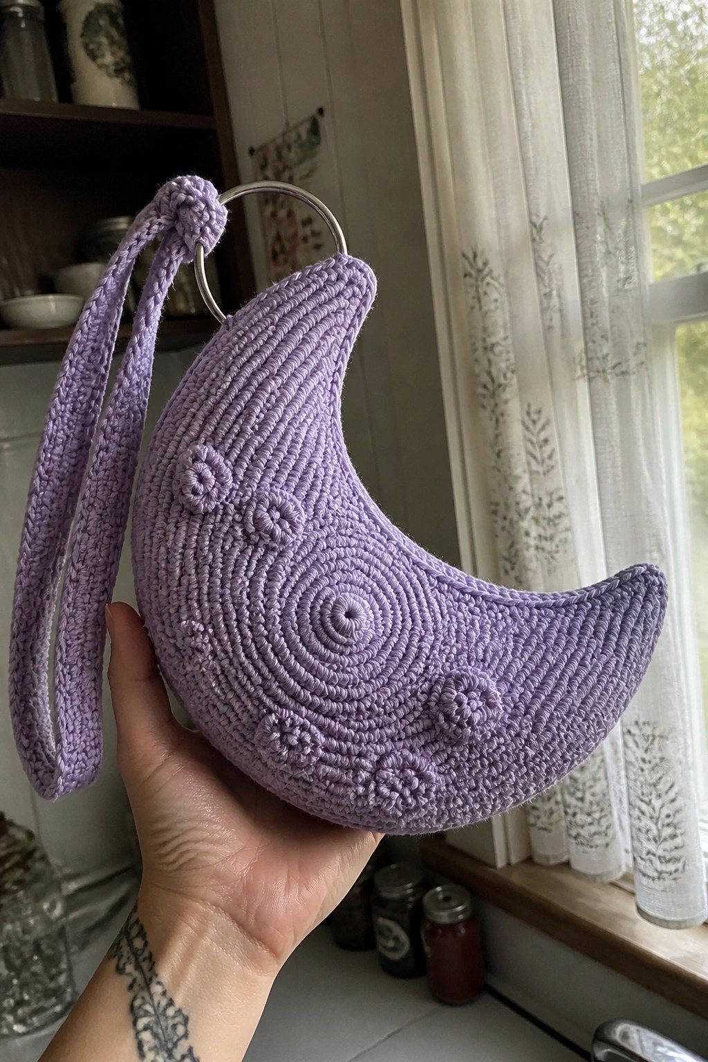Hand holding purple crocheted crescent moon bag with metal ring and strap.