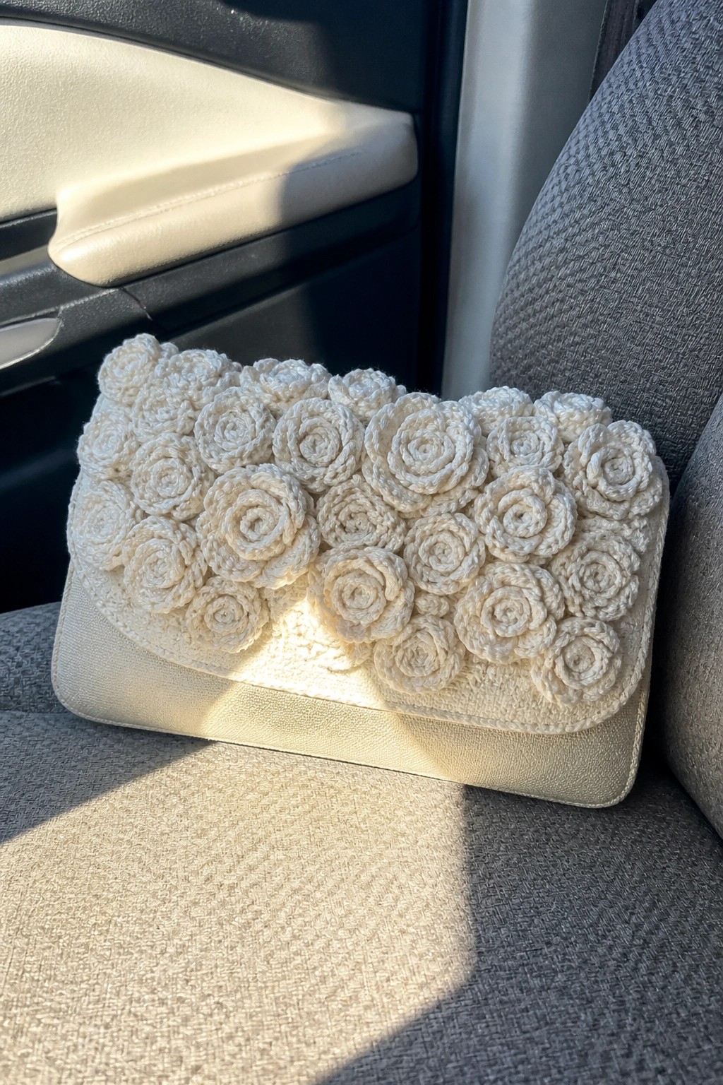 Cream crocheted clutch with rose motifs on gray car seat