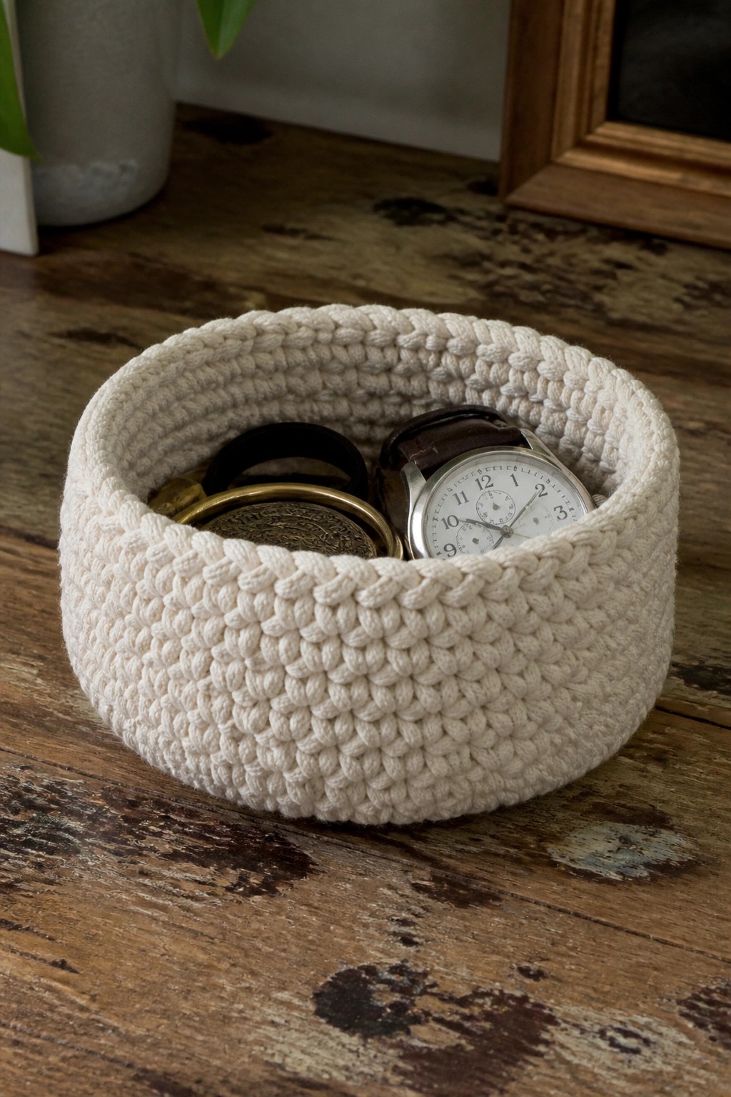 Cream crocheted basket with watch and bracelets on rustic wood table.
