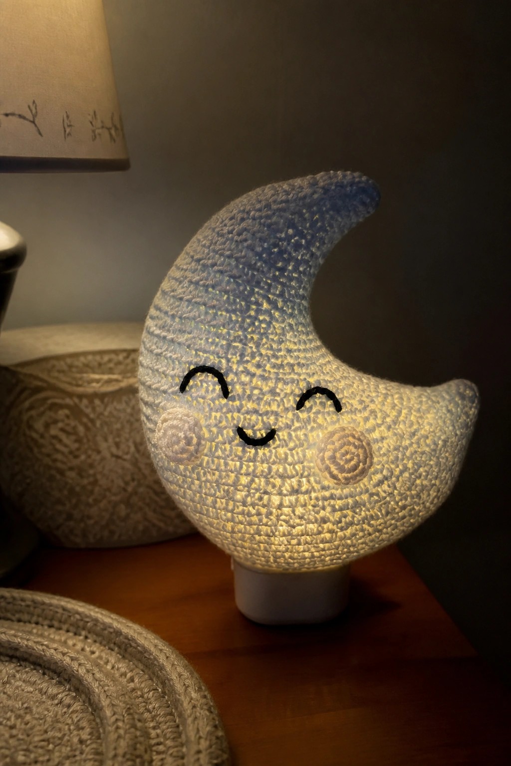 Glowing crocheted crescent moon nightlight with smiling face on wooden table