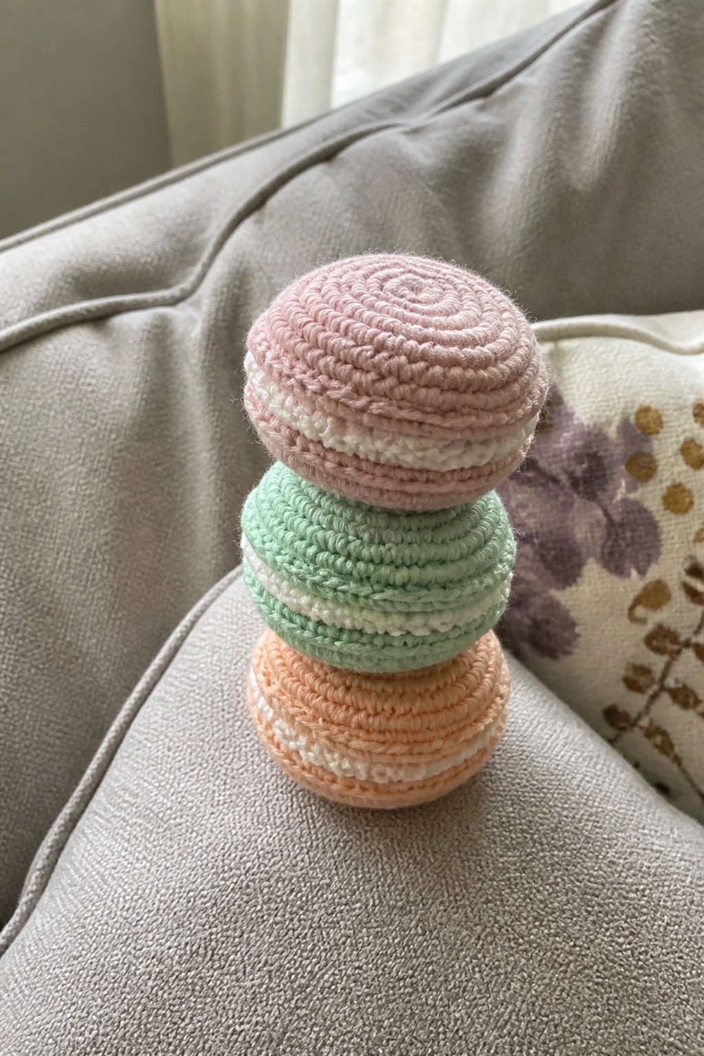 Stacked crocheted macarons in pink, mint green, and peach on gray couch