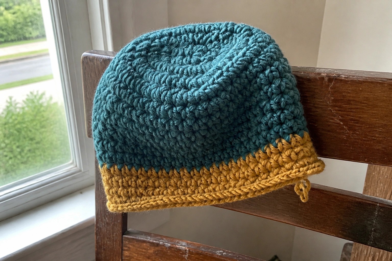 Two-tone knitted beanie in teal and mustard on wooden bench by window