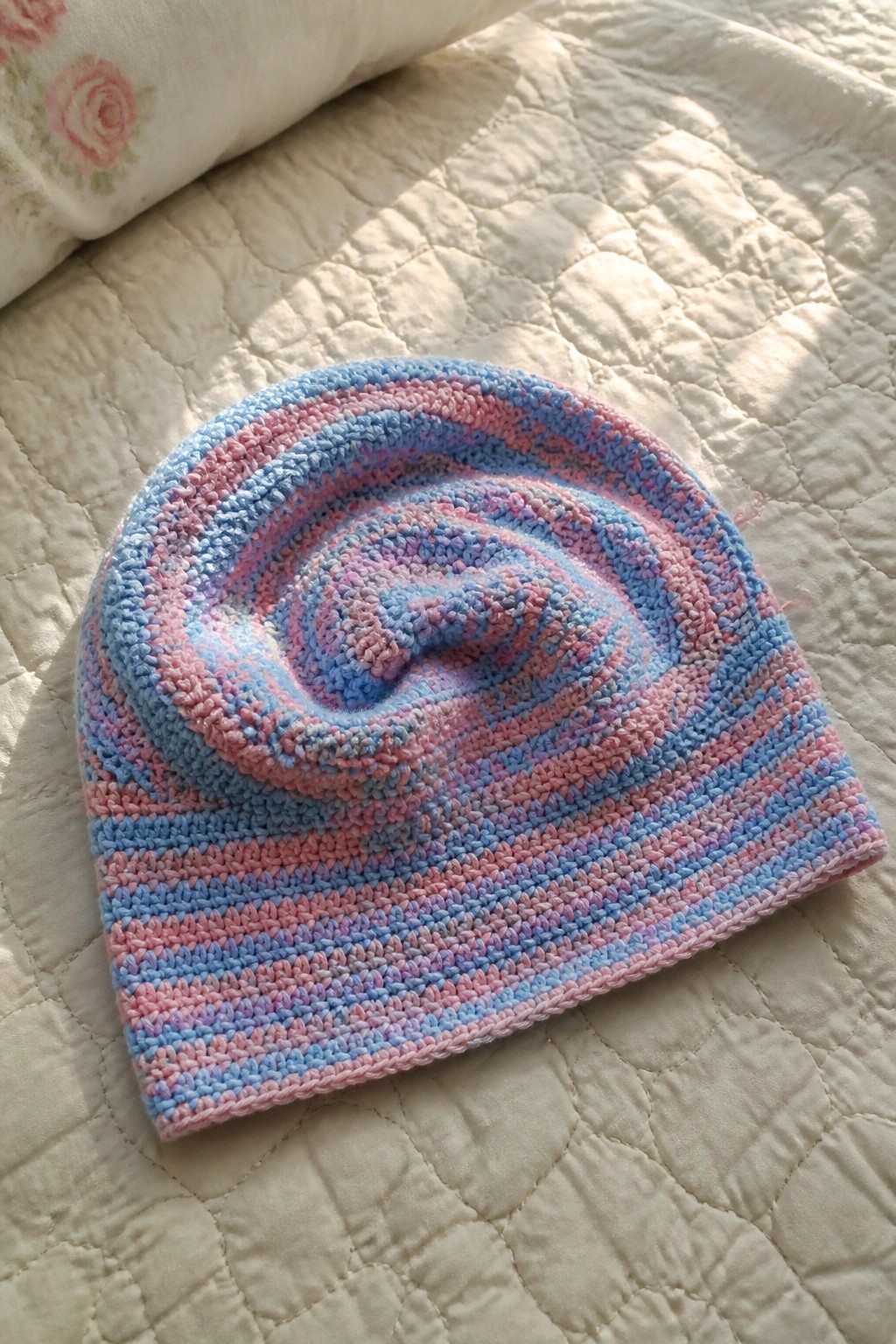Striped pink blue purple knitted beanie with swirled top on white quilt