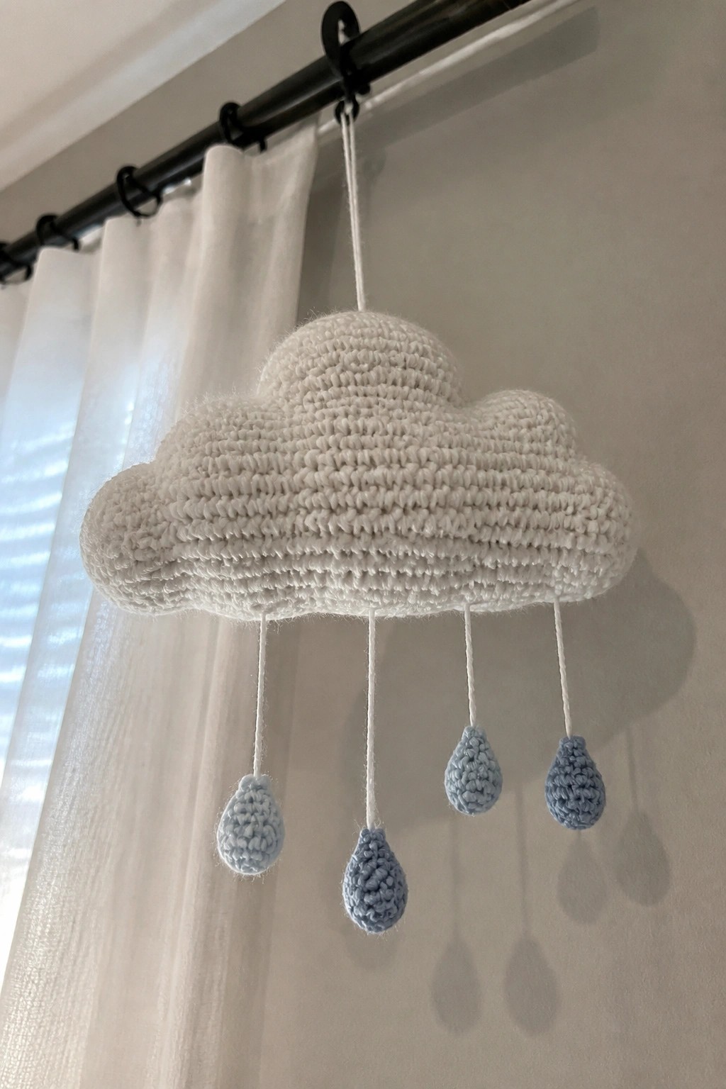 A white crocheted cloud with four light blue crocheted raindrops hanging from strings.
