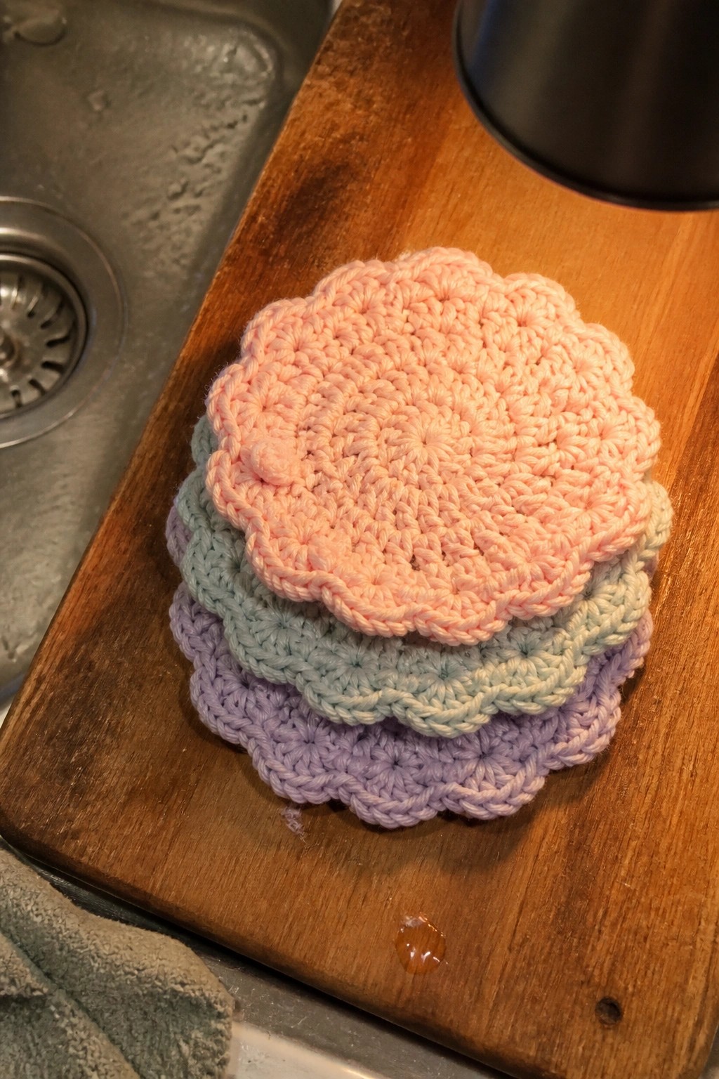 Stack of pastel pink, blue, and purple crocheted coasters on wooden board