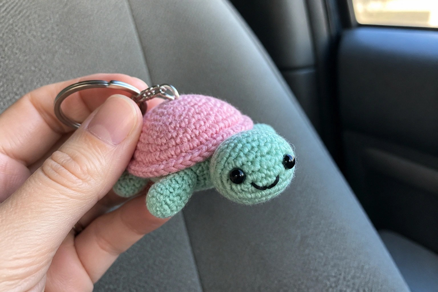 Hand holding mint green crocheted turtle keychain with pink shell and keyring
