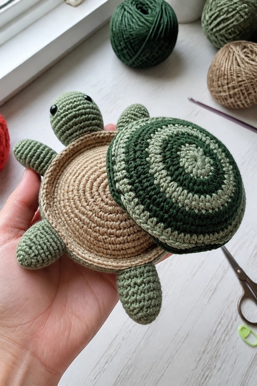 Hand holding crocheted turtle with green striped shell, beige base, and limbs.