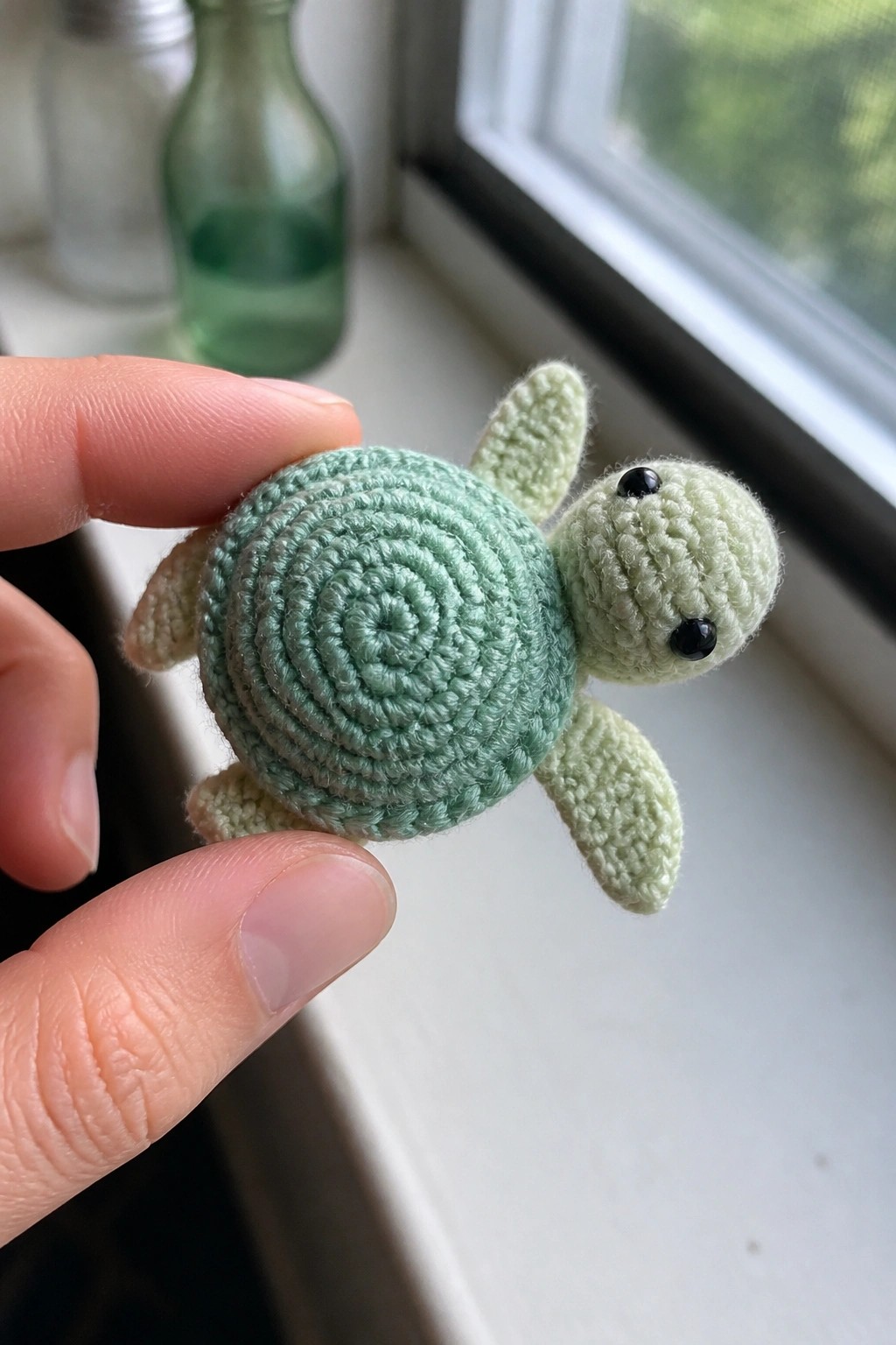 Hand holding small mint-green crocheted sea turtle with spiral shell and black eyes