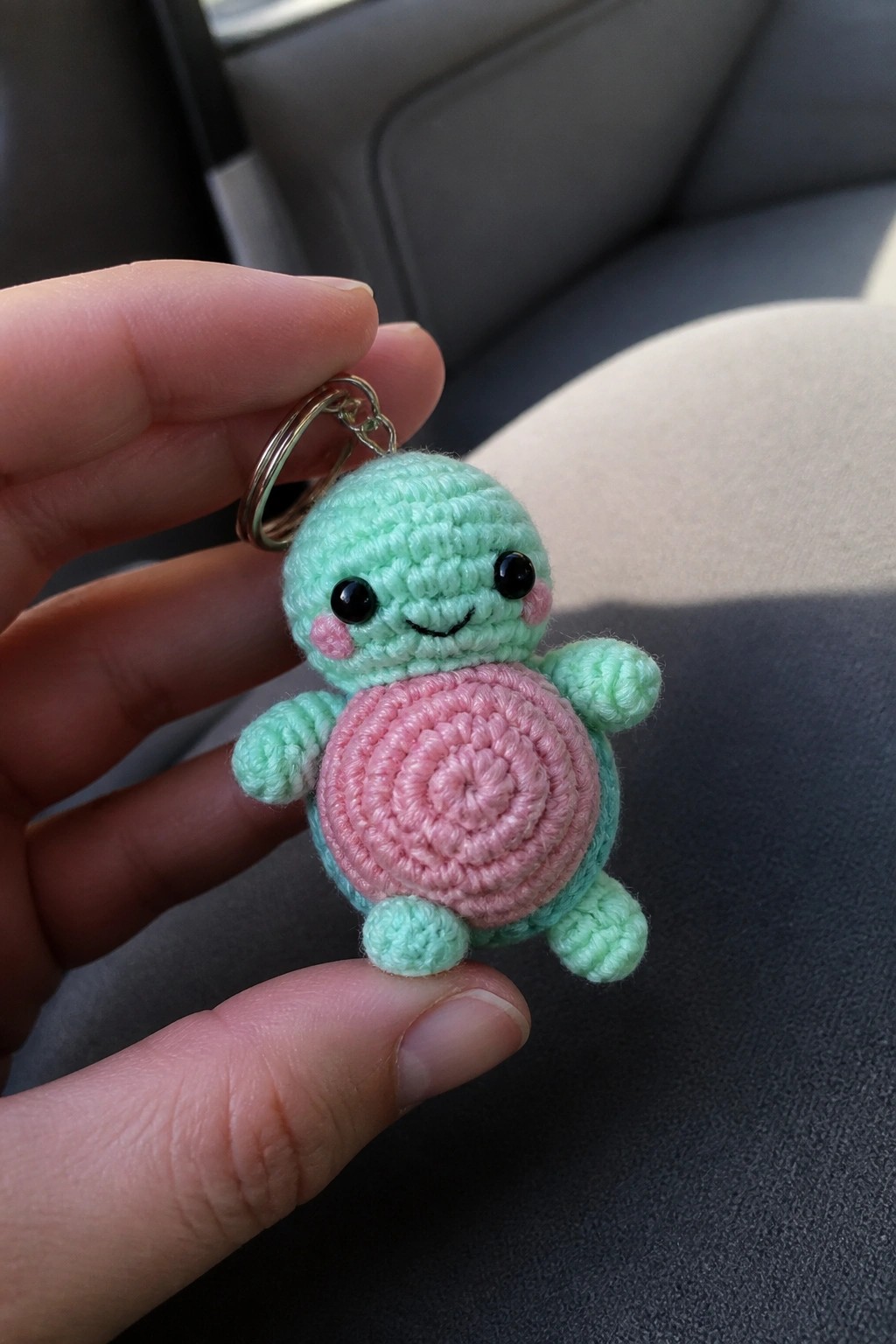 Hand holding mint green crocheted turtle keychain with pink shell and keyring