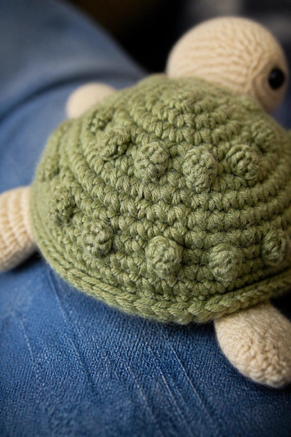 Green crocheted turtle with beige head and legs on blue denim jeans