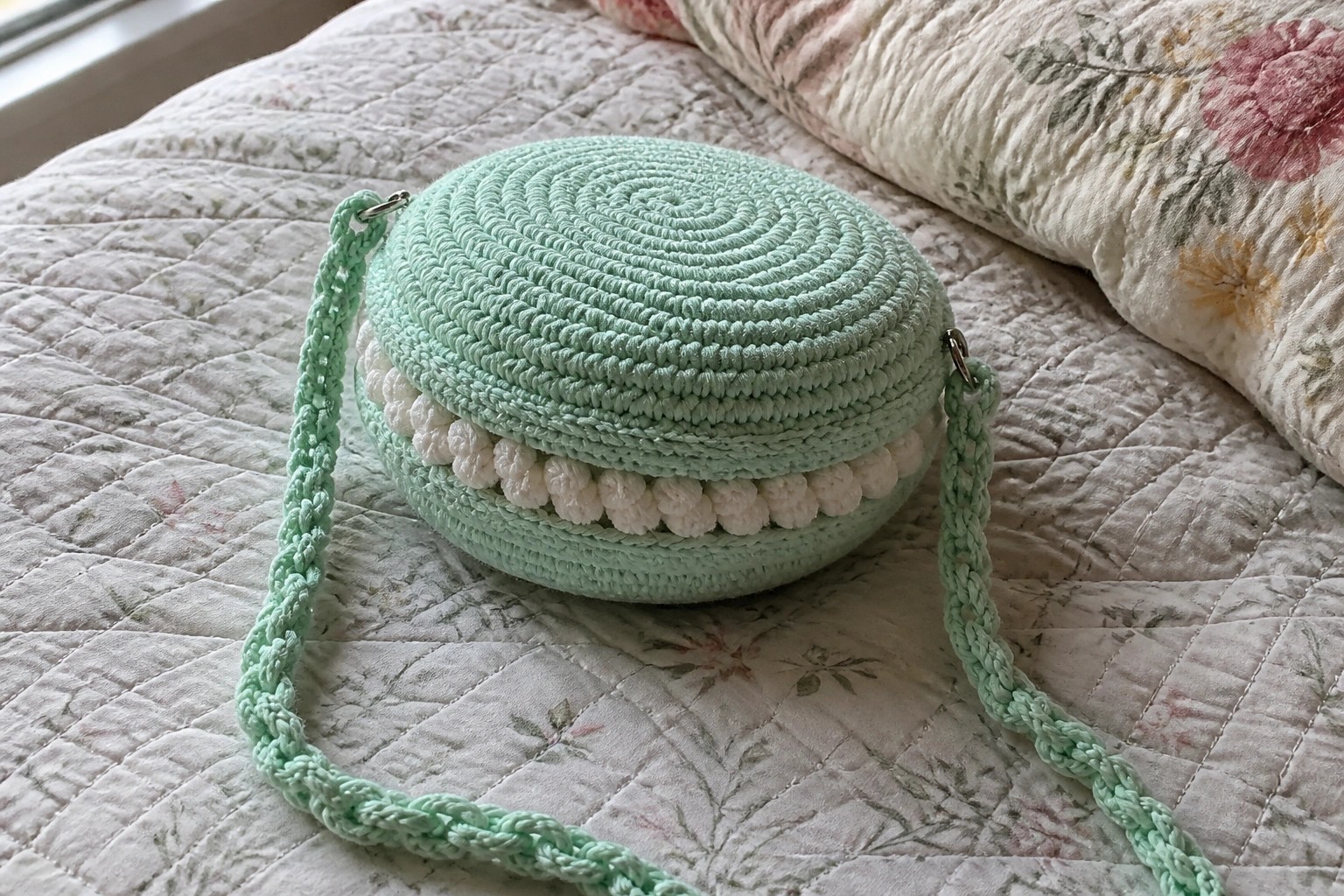 Mint green crocheted macaron purse with white filling on floral quilted bed