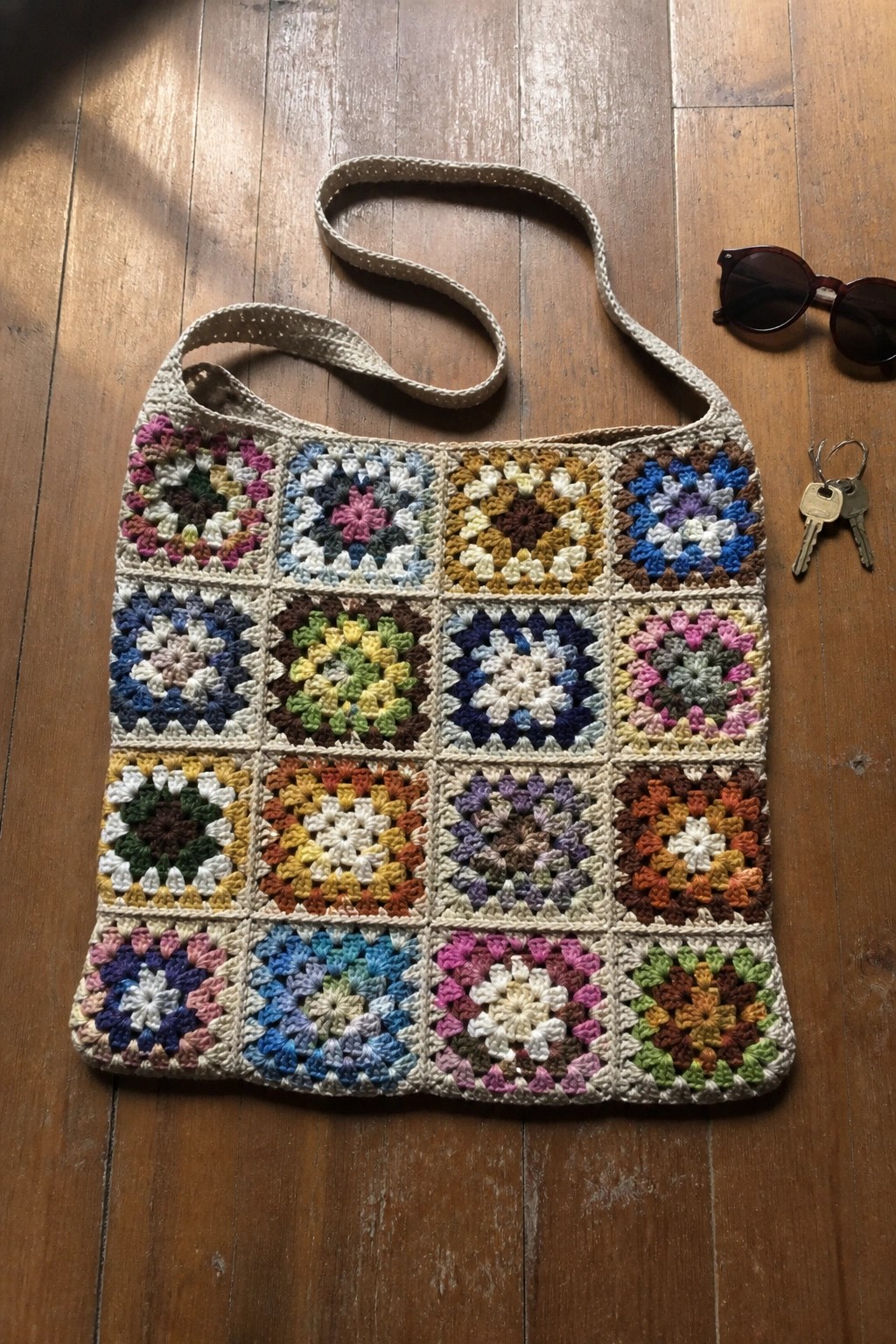 Colorful granny square crochet tote bag on wooden floor with sunglasses and keys.