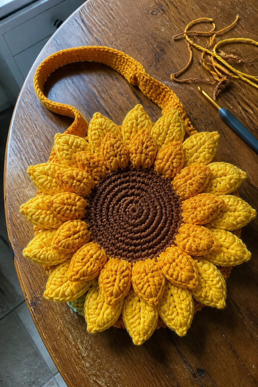 Crocheted sunflower bag with yellow petals, brown center, and strap on wooden table