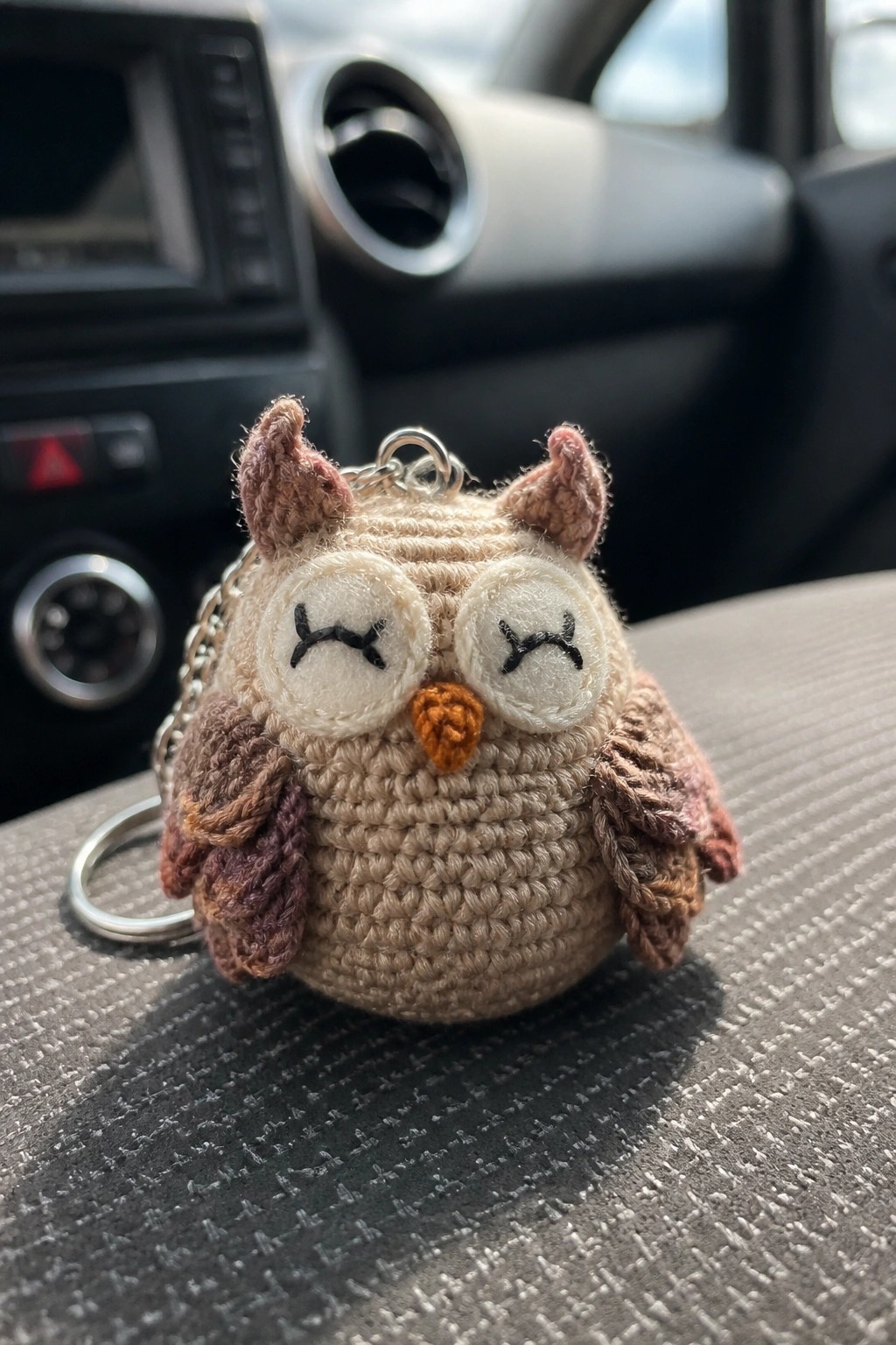 Crocheted beige owl keychain with closed eyes and brown wings on car seat