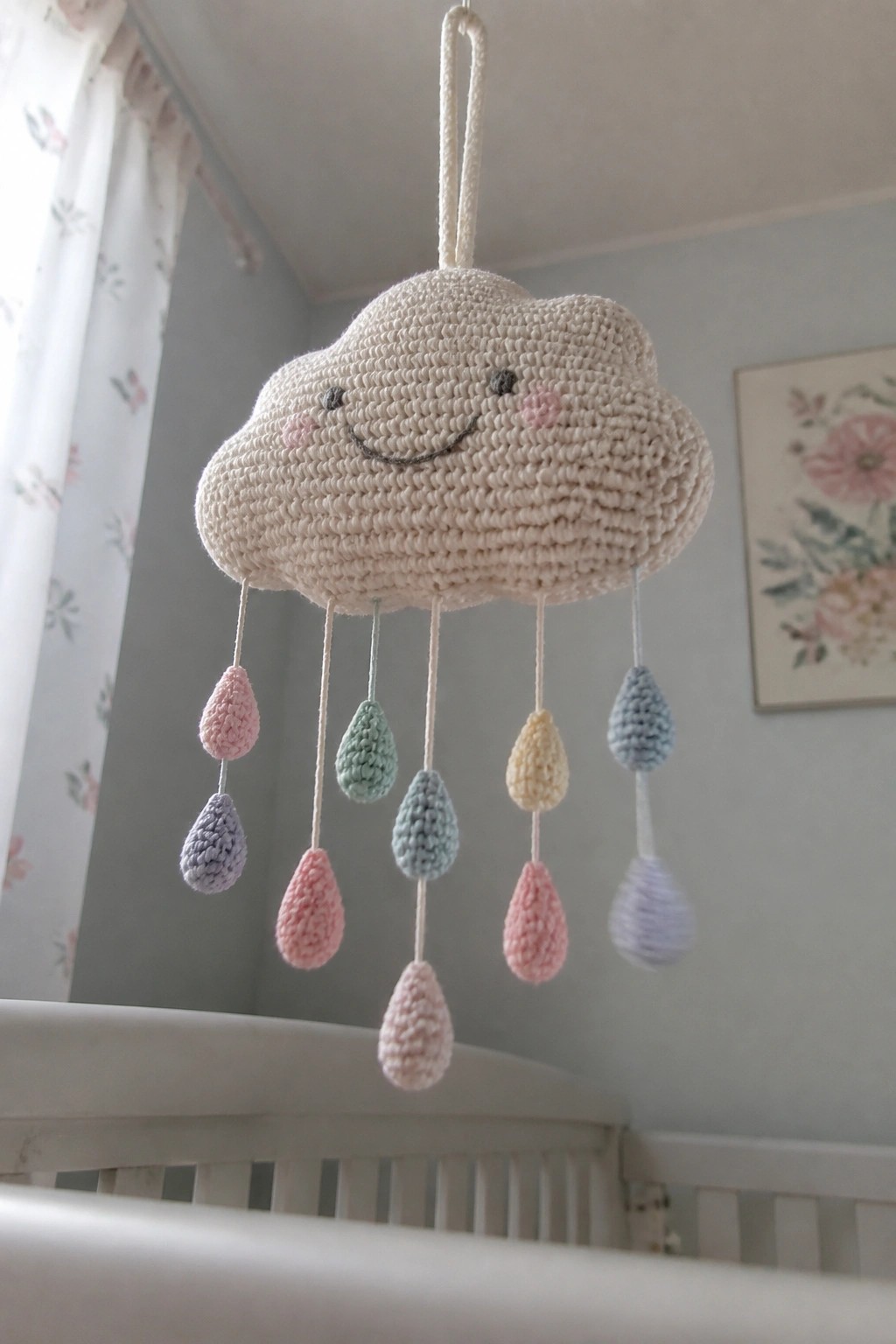 Crocheted smiling cloud mobile with pastel raindrops above white crib