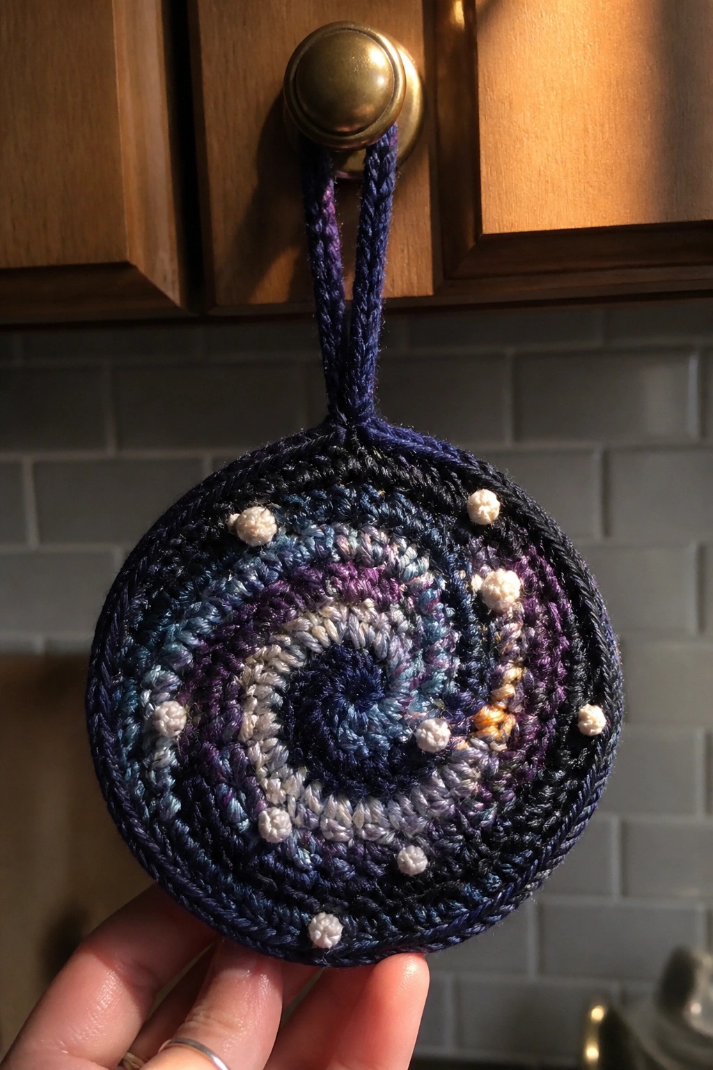 Hand holding crocheted galaxy-themed circle with white stars from brass knob