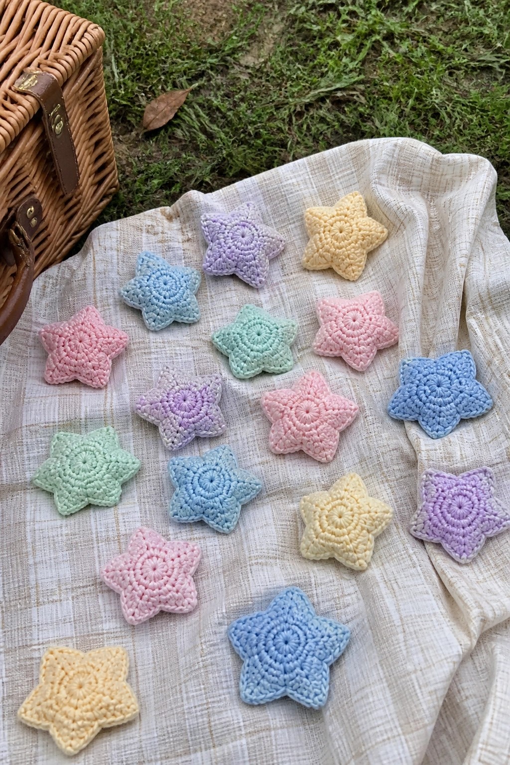 Pastel crocheted stars scattered on fabric beside wicker picnic basket on grass