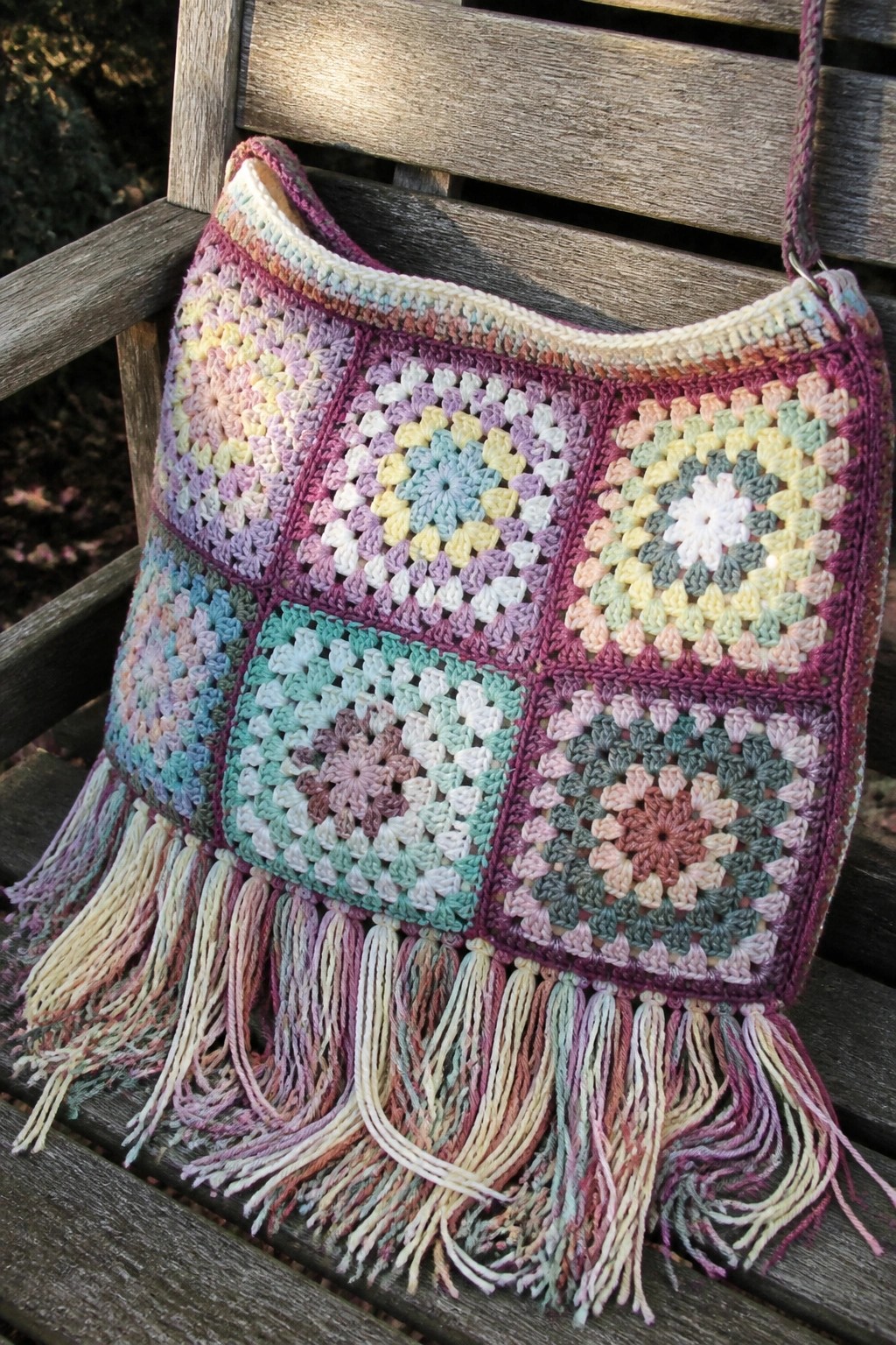 Colorful crocheted granny square bag with long fringes on wooden bench