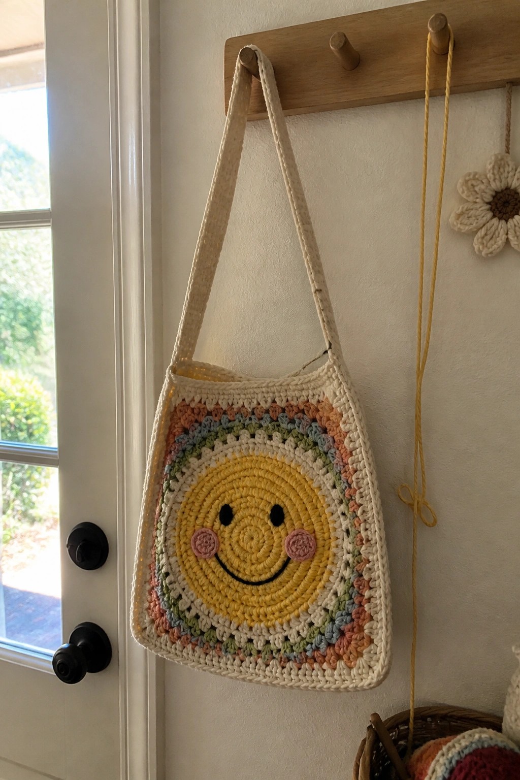 Crocheted smiley face bag with colorful borders hanging on wooden peg hook