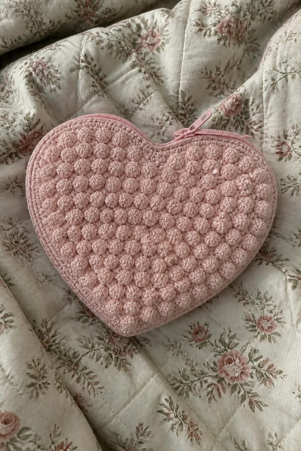 Pink heart-shaped crocheted pouch with zipper on floral quilted fabric
