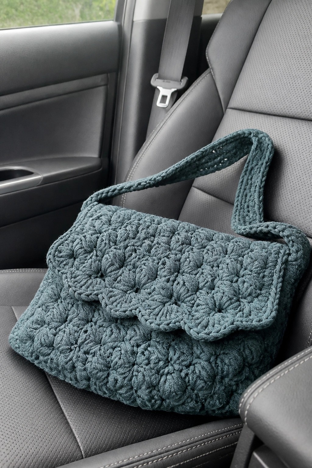 Teal crocheted handbag with flap on black leather car seat