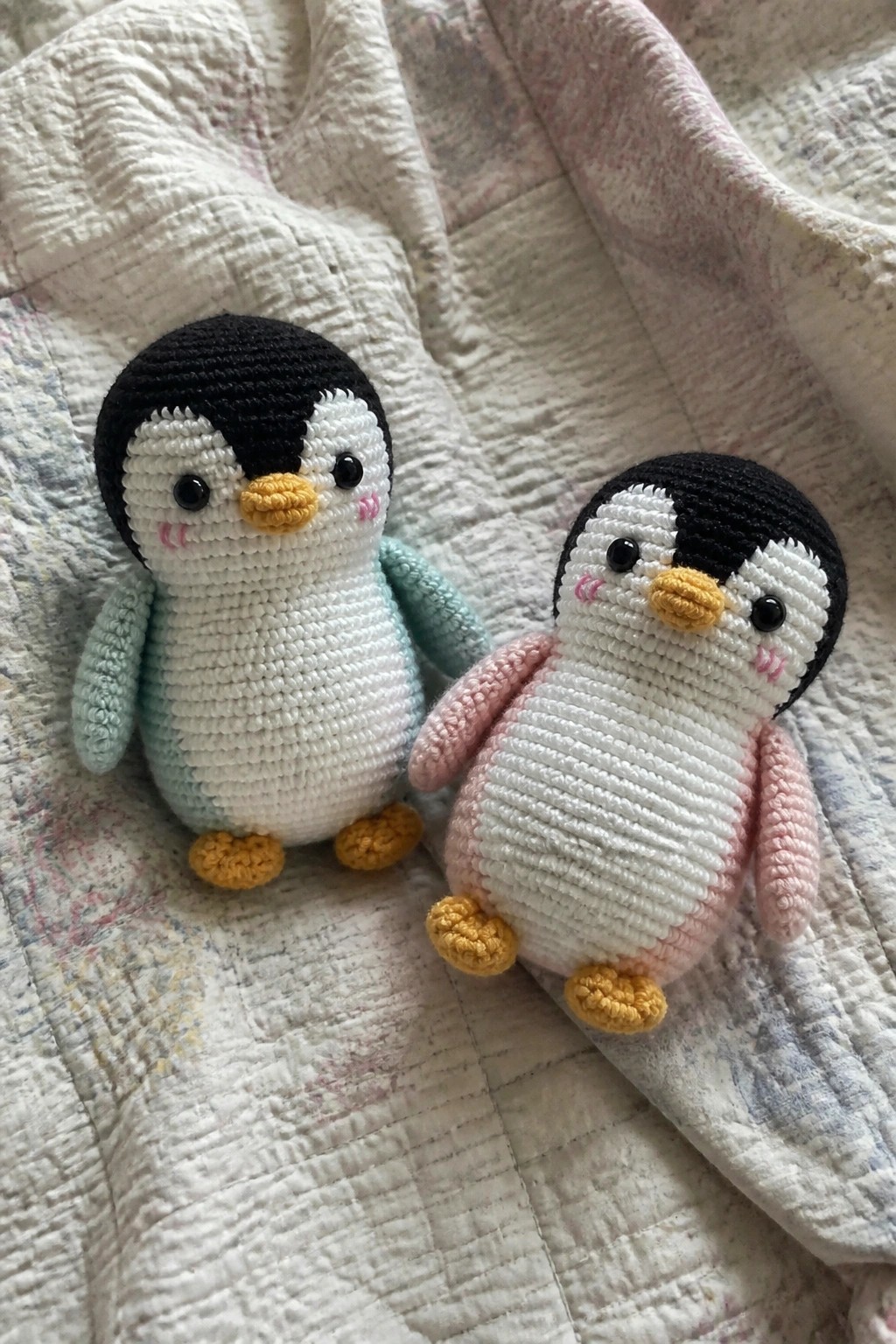 Two crocheted penguins with mint and pink wings on a floral quilted blanket