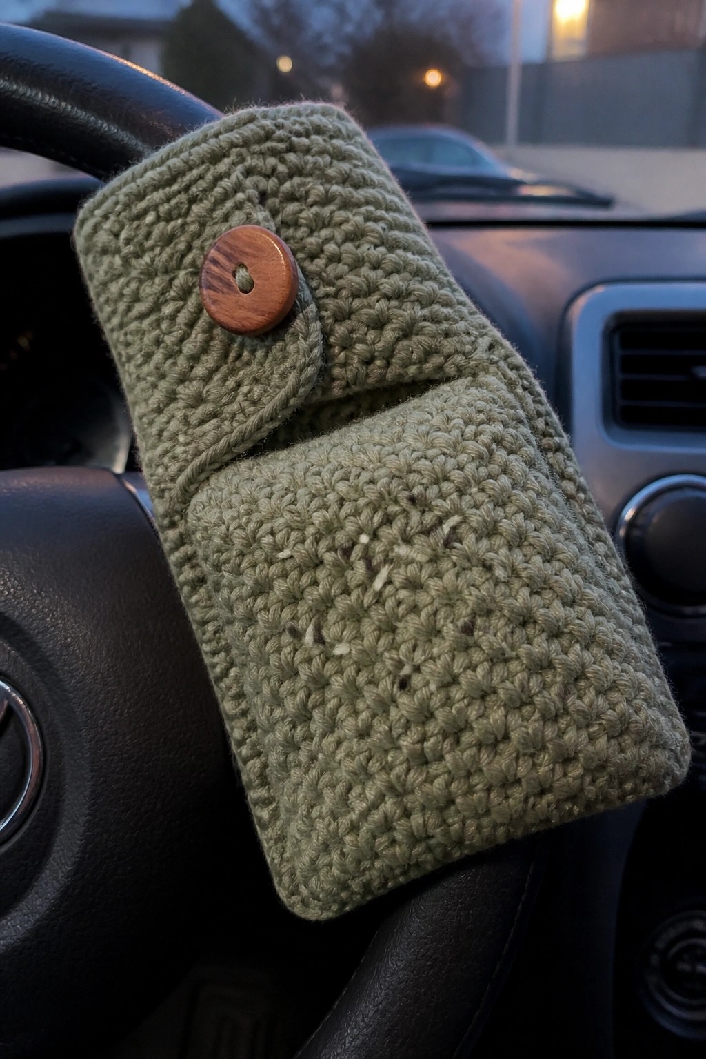 Green crocheted pouch with wooden button on car steering wheel