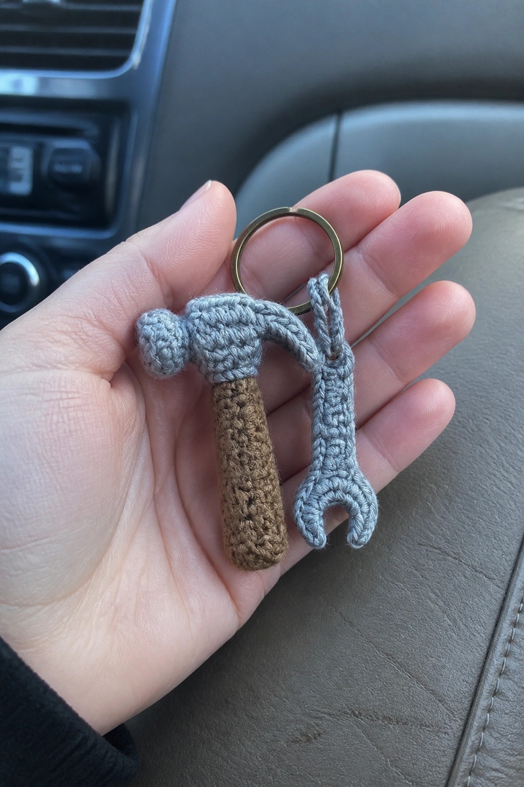 Hand holding crocheted gray hammer and wrench keychain inside car interior