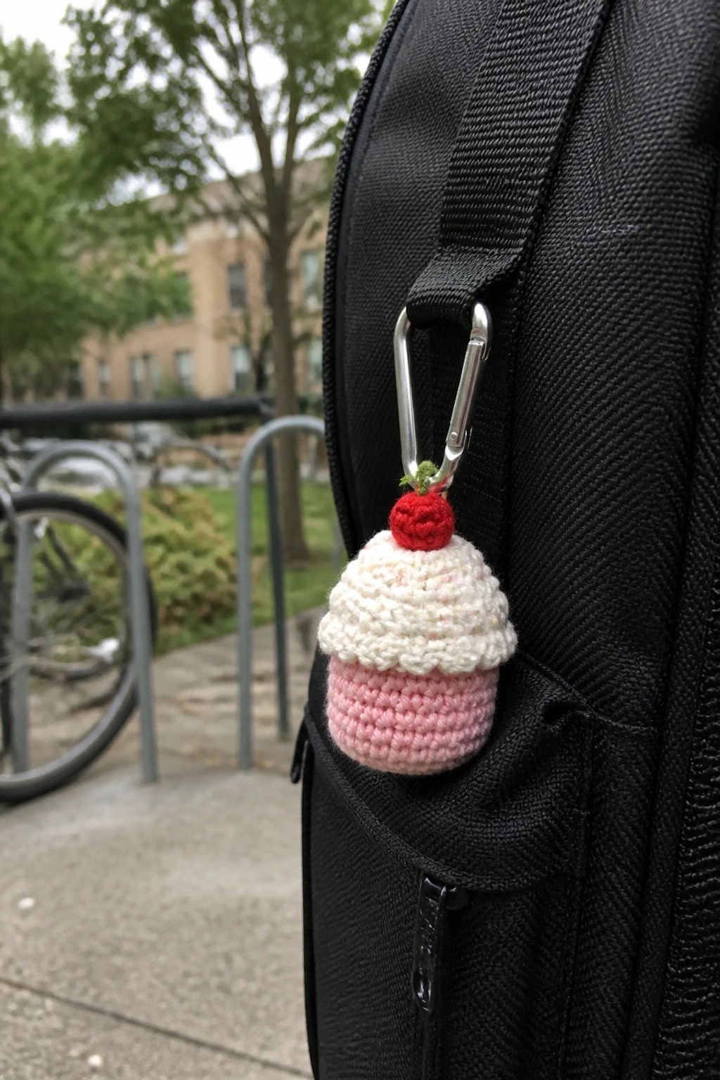 Crocheted pink cupcake keychain with red cherry on black backpack carabiner