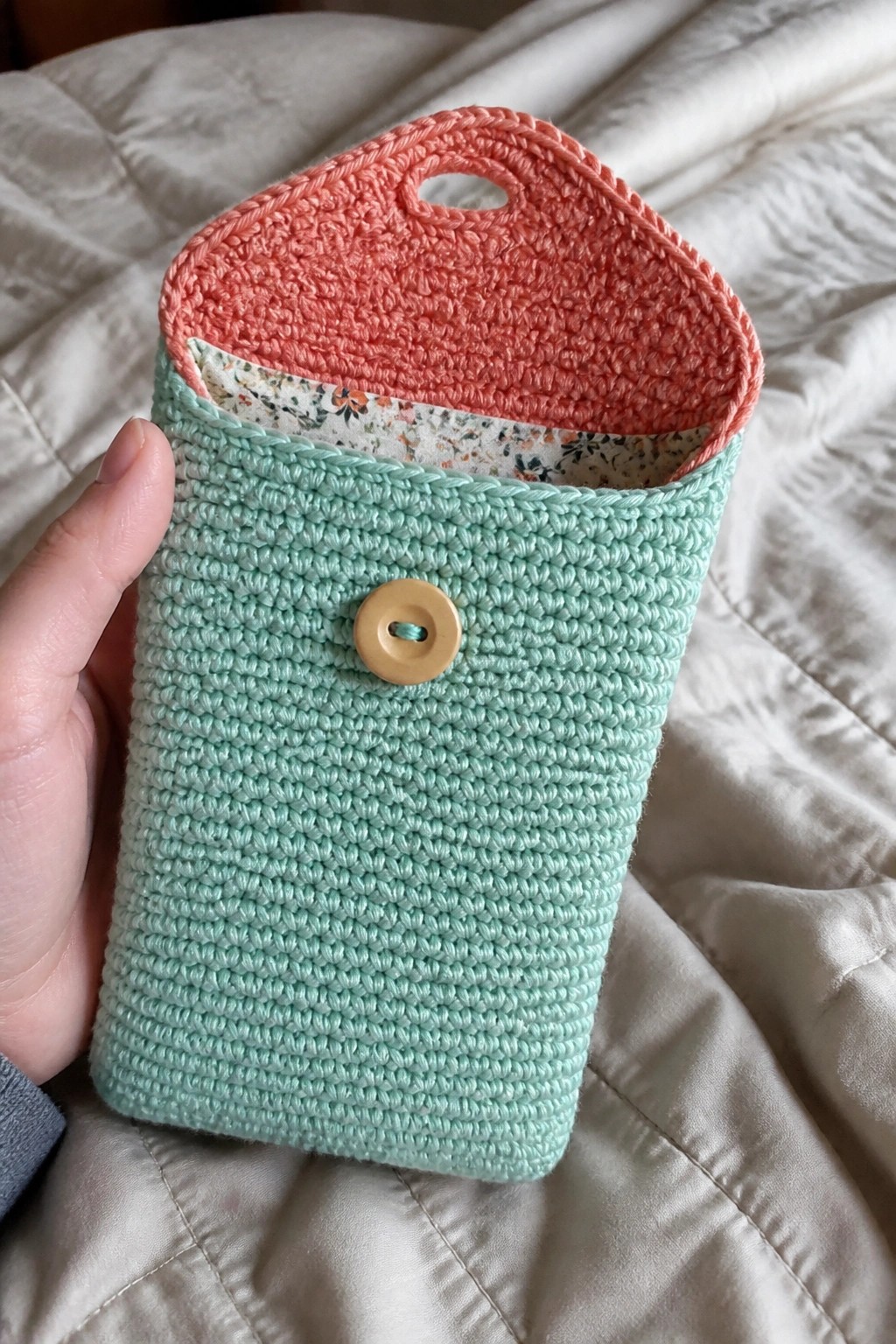 Hand holding mint green crocheted pouch with coral flap, button, and floral lining