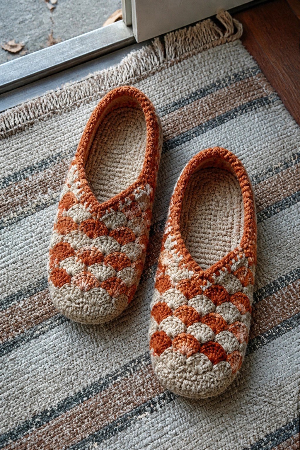 Pair of orange and beige crocheted slippers on a striped woven rug