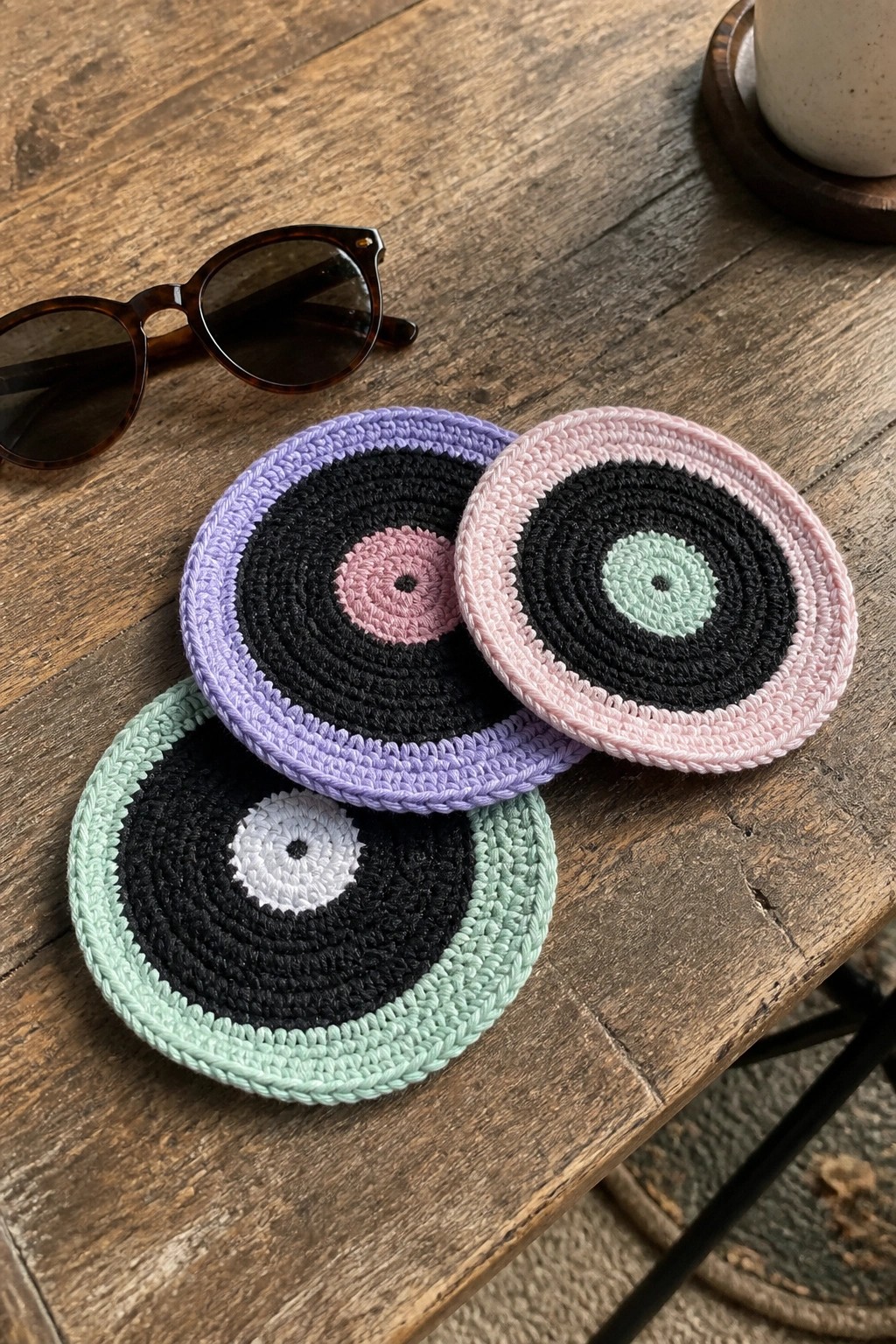 Three pastel crocheted vinyl record coasters on wooden table with sunglasses
